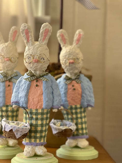 Decorative rabbit figurines with checkered outfits and glasses on a wooden surface.